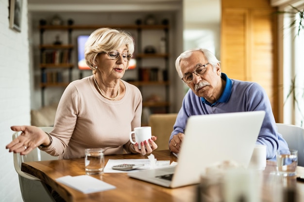 Senior couple talking while analyzing their home budget and using computer at home