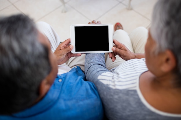 リビングルームに座っている間デジタルタブレットを使用して年配のカップル