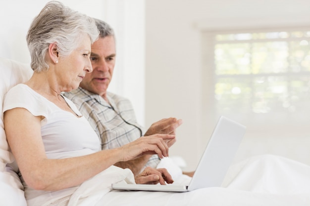 Senior couple using laptop sitting on the bed