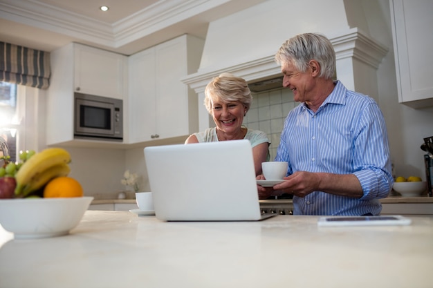 Senior couple using laptop while having tea in kitchen