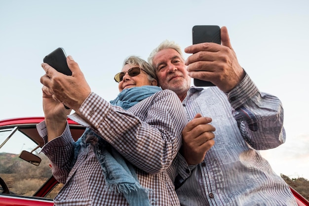 Photo senior couple using smart phones while standing by car