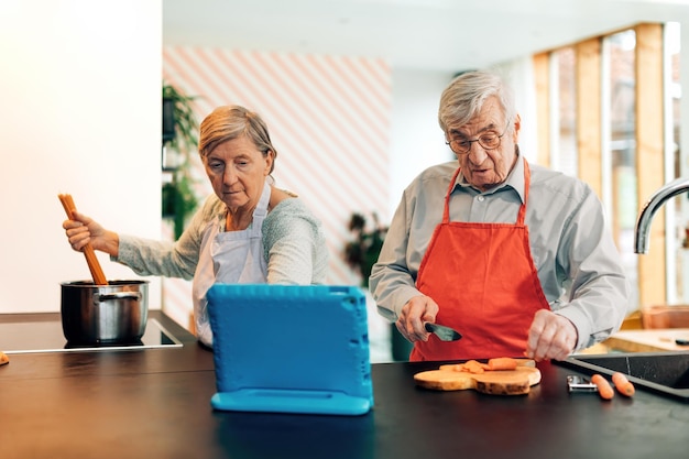 Senior couple using technology for cooking elder people using\
on line blog tutorial recipes