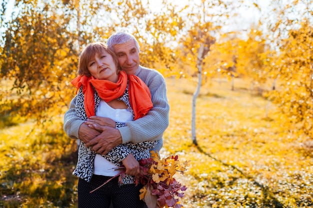 Senior couple walking in autumn forest Middle aged man and woman hugging 