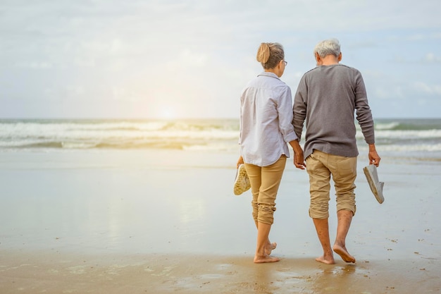 Senior couple walking on the beach holding hands at sunrise, plan life insurance at retirement concept.