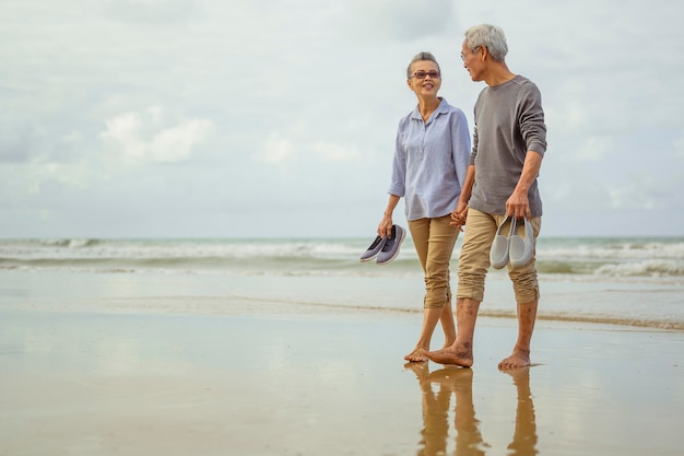 Старшие пары гуляют на пляже, держась за руки на восходе солнца, планируют страхование жизни на пенсии.