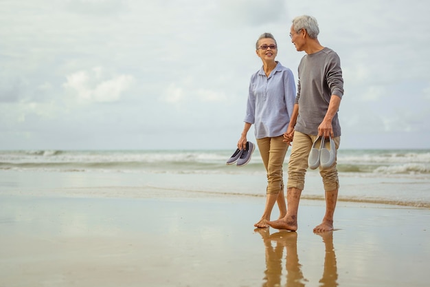 Senior couple walking on the beach holding hands at sunrise, plan life insurance at retirement concept.