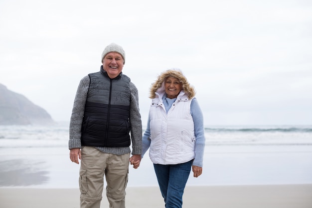 Пожилая пара прогулки с взявшись за руки на пляже