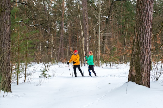 雪の降る冬の森でノルディックウォーキングポールを持って歩く年配のカップル