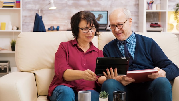 Senior couple waving at tablet during a video call. Elderly people sitting on sofa.