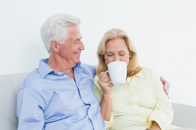 Senior couple with coffee cup sitting on sofa