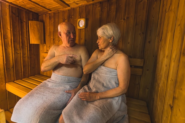 Старшая пара с полотенцами разговаривает в сауне.