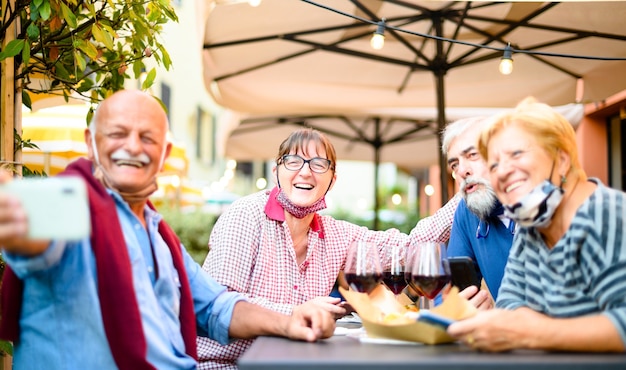 Foto coppie senior che prendono selfie al bar ristorante con maschere facciali