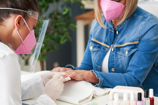 senior dame met een masker in manicure salon