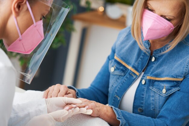 senior dame met een masker in manicure salon