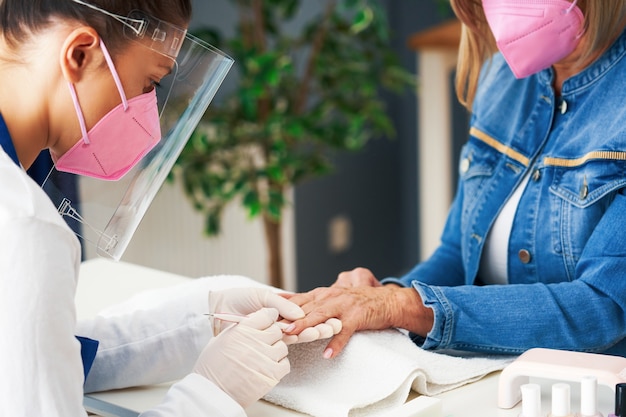 senior dame met een masker in manicure salon