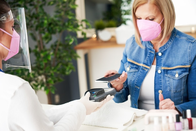 senior dame met een masker in manicure salon