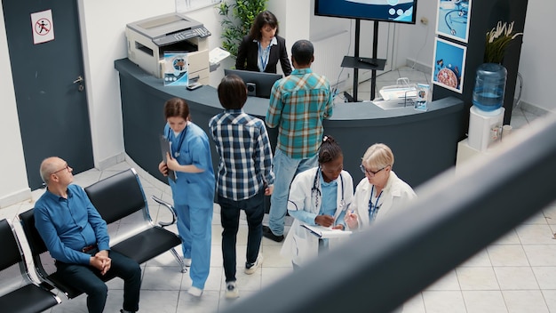 Senior doctor and african american medic talking in hospital\
reception lobby, checking healthcare report to consult patients\
with disease. medical staff with expertise in waiting room\
area.