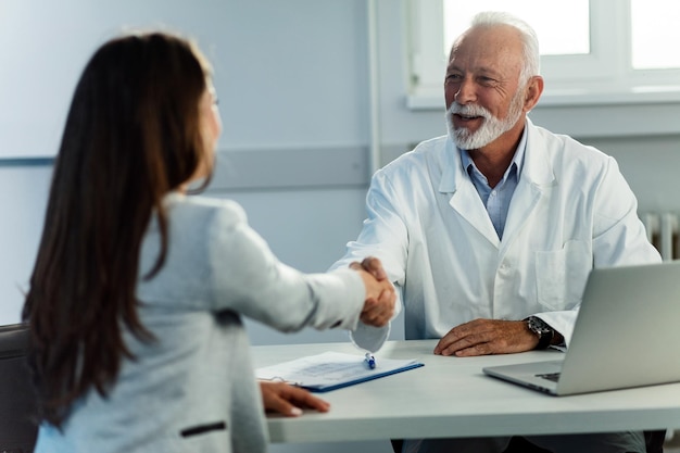 Senior doctor shaking hands with female patient while meeting at doctor's office