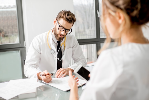 Senior doctor with young female assistant working with medical documents at the white office interior