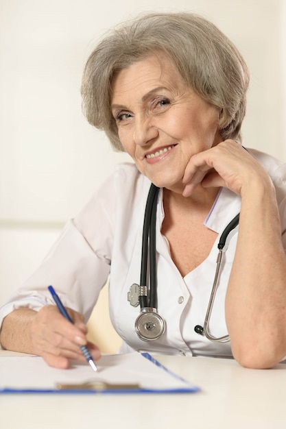 Senior doctor woman sitting at table on white background