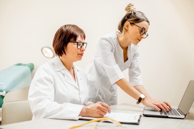 Senior doctor and young woman assistant working together with laptop and documents in the gynecological office