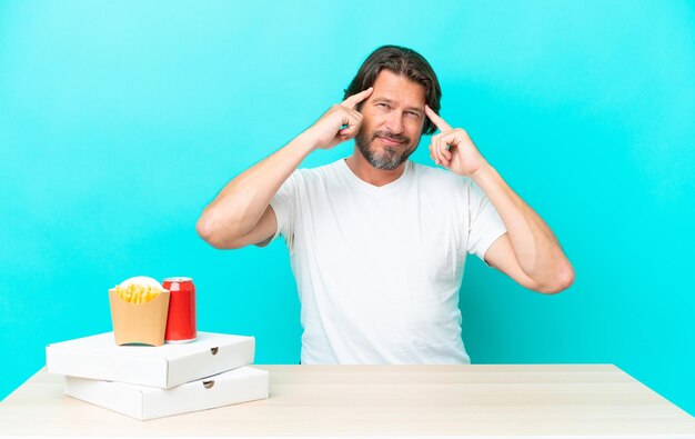 Uomo olandese anziano che mangia fast food seduto a un tavolo con dubbi e pensieri