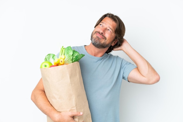 Senior dutch man holding grocery shopping bag over isolated background having doubts