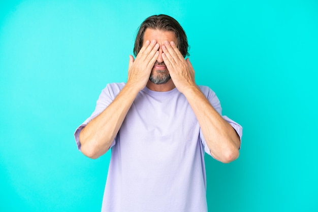 Senior dutch man isolated on blue background covering eyes by hands