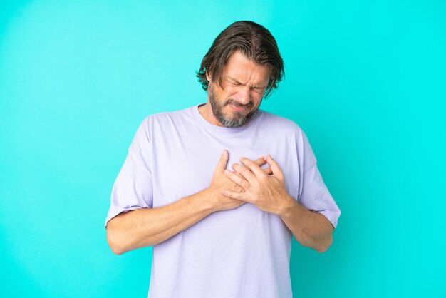 Senior dutch man isolated on blue background having a pain in the heart