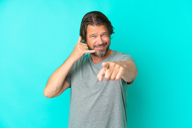 Senior dutch man isolated on blue background making phone gesture and pointing front