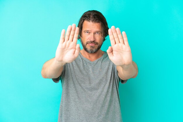 Senior dutch man isolated on blue background making stop gesture and disappointed