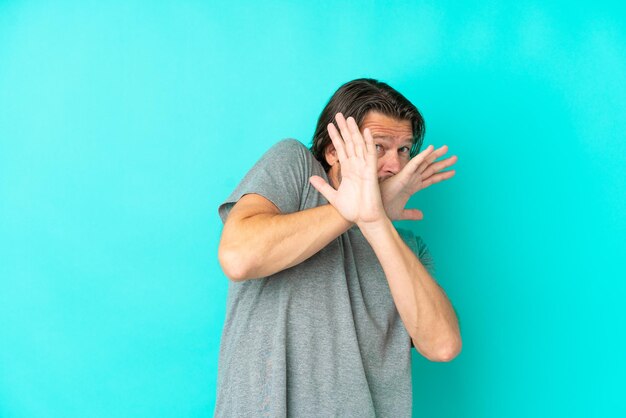 Senior dutch man isolated on blue background nervous stretching hands to the front