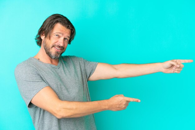 Photo senior dutch man isolated on blue background pointing finger to the side and presenting a product