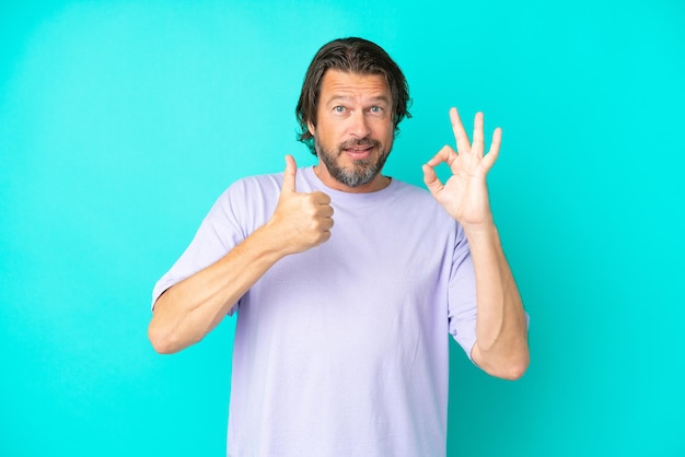 Senior dutch man isolated on blue background showing ok sign and thumb up gesture