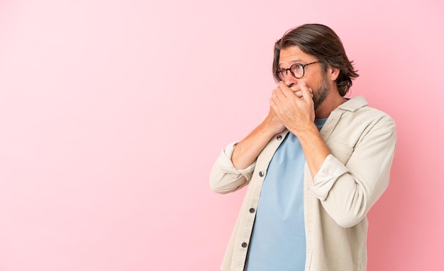 Senior dutch man isolated on pink background covering mouth and looking to the side