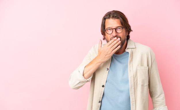 Uomo olandese anziano isolato su sfondo rosa felice e sorridente che copre la bocca con la mano