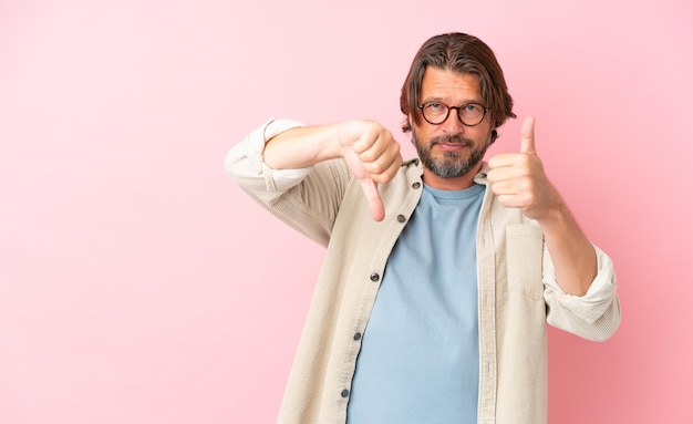 Senior dutch man isolated on pink background making good-bad sign. Undecided between yes or not