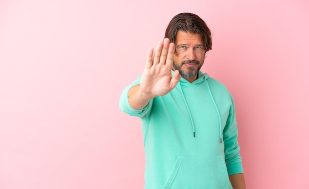 Senior dutch man isolated on pink background making stop gesture