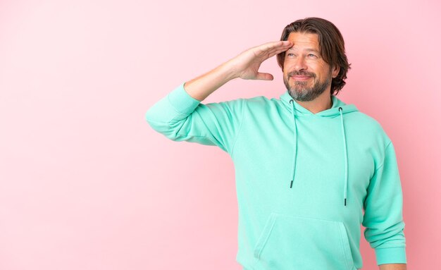 Senior dutch man isolated on pink background saluting with hand with happy expression