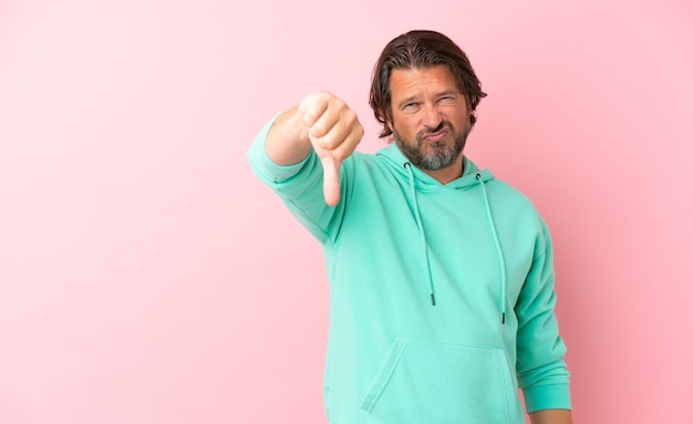 Senior dutch man isolated on pink background showing thumb down with negative expression