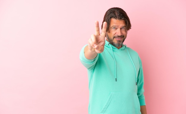 Senior dutch man isolated on pink background smiling and showing victory sign