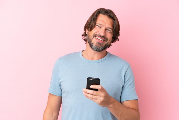 Senior dutch man isolated on pink background using mobile phone