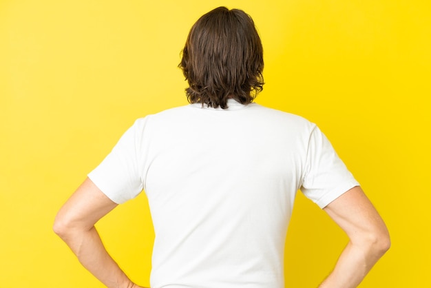 Senior dutch man isolated on yellow background in back position