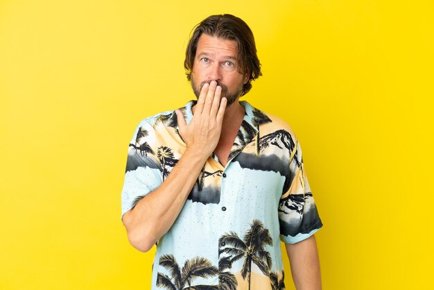 Senior dutch man isolated on yellow background covering mouth with hand