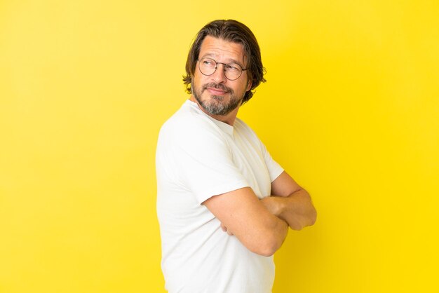 Senior dutch man isolated on yellow background looking to the side and smiling