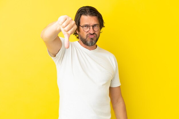 Senior dutch man isolated on yellow background showing thumb down with negative expression