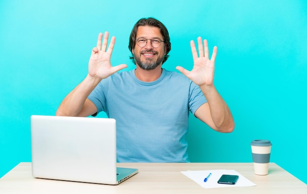 Senior dutch man in a table with a laptop isolated on blue background counting nine with fingers