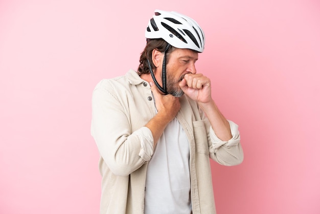 Senior dutch man with bike helmet isolated on pink background is suffering with cough and feeling bad