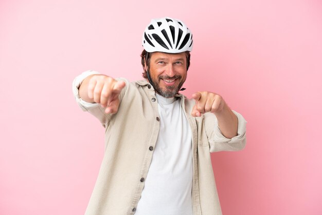 Senior dutch man with bike helmet isolated on pink background points finger at you while smiling