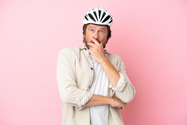 분홍색 배경에 격리된 자전거 헬멧을 쓴 네덜란드 노인은 오른쪽을 바라보는 동안 놀라고 충격을 받았습니다.